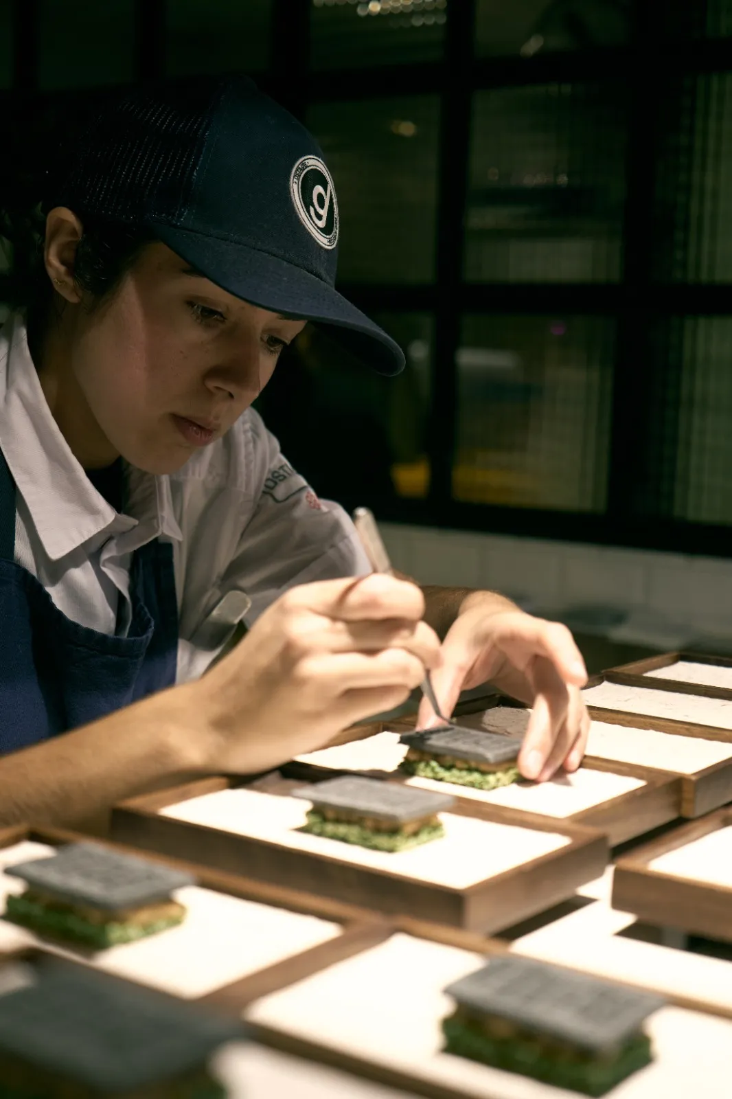 Emplatando un postre con pinzas, pieza a pieza, en el obrador.